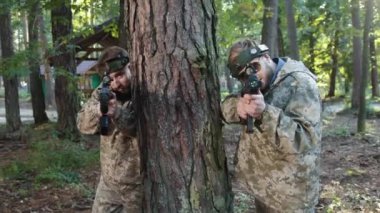 Eğitim ortamı, sahte savaş, savaş etiketi. Yoğun ormanda kamufle olmuş oyuncular ağaçların arkasına çömelmiş, paintball silahlarıyla taktiksel bir oyun oynuyorlar..