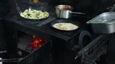 Kızarmış sebzeler, mutfak aroması, kızartma tekniği. Ocakta, sebzelerle dolu tavada, sosla kaynayan tencerede, ve başka bir tavada kızartma pişirme işlemi tasvir ediliyor..
