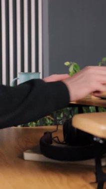 Laptop, dizüstü bilgisayar, mavi masa. Yakın planda, erkek eller dizüstü bilgisayarı kavrıyor, mavi kupa ahşap masada dinleniyor ve yeşil bitki arka planda çizgili duvara dayanıyor, dikey video.