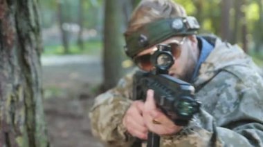 Zayıf, nişan alınmış, düşman hedefi. Sportif kamuflaj kıyafeti giyen ve kafasındaki işaretle ağaca yaslanmış bir adam, kasıtlı olarak lazer tabancasını doğrultuyor ve ormanda düşmanını vuruyor..