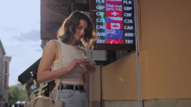Dolarlar, para transferi, döviz kuru. Kadın, uluslararası bayrakları ve para kodlarını gösteren dijital panodaki paraları sayıyor..