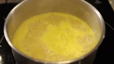 Sarı sıvı, kaynayan sıvı, paslanmaz ot. Yakın çekim sarı sıvı paslanmaz çelik kapta kaynıyor, aktif yemek, muhtemelen sos ya da et suyu, tencere fırının üstünde duruyor, canlı sarı renkli.