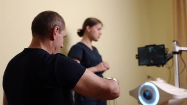 Rehabilitasyon cihazları, robotik terapi, kol rehabilitasyonu. Klinik ortamda robotik teknolojiden yararlanan fizyoterapistin uzmanlığından kol terapisi gören bir adam..