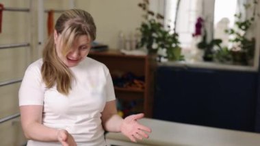 Gülümseyen antrenör, sağlık koçluğu, terapi koçluğu. Beyaz tişörtlü gülümseyen bayan antrenör rehabilitasyon merkezindeki seans sırasında el hareketleriyle iletişim kurar..