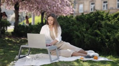 Sakura Parkı, Dijital Göçebe, Çalışma Ortamı. Kadın, huzurlu parktaki sakura ağaçlarının arasına kurulmuş dizüstü bilgisayarıyla emek harcıyor..