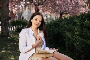 Huzurlu ortam, doğa kaçışı, rahatlatıcı sahne. Genç kadın kiraz çiçeklerinin altında otururken, elinde çiçeklerle ve yanında atıştırmalıklarla, huzurlu bir sahne beliriyor..