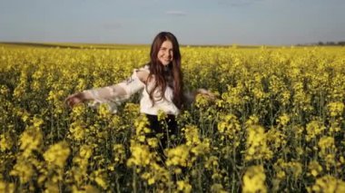 Halk nakış işliyor, gökyüzü açık, çiçek açıyor. Çiçekli sarı kanola tarlasında, neşeli bir kadın geleneksel nakış işleyerek açık mavi gökyüzünün altında neşeleniyor..