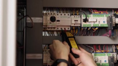 Elektrikçi testleri, elektrik bağlantıları, elektrik tamiratları. Elektrik bağlantılarını renkli kablolarla devre kesici panelde test etmek için çoklu metre kullanan yakın çekim elektrikçisi.