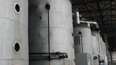 Büyük tanklar, büyük bir depo, tesisat boruları. Geniş endüstriyel ortamda, dizilim boruları ve kanallarla birbirine bağlı birkaç büyük metal depolama tankı düzenlenmiştir..
