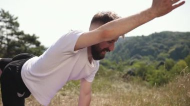 Yoga dengesi, farkındalık pratiği, doğa çevresi. Beyaz tişörtlü ve siyah şortlu genç adam doğa tarafından çevrili çimenlik alanda yoga dengesi pozisyonunda duruyor. Farklılık, denge