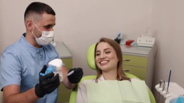 Dişçi gösterileri, dişçi uzmanlığı, diş bilgisi. Yüz maskesi takan erkek dişçi, kadın hasta ve diş hekimleriyle konuşurken diş aletleri ve modelini gösteriyor.