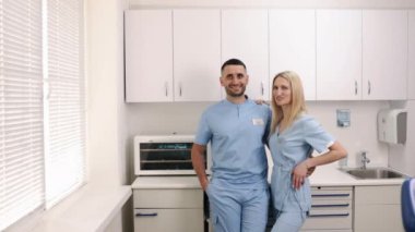 Diş hekimleri, beyaz dolaplar, klinik ortamları. Mavi önlüklü iki dişçi modern klinikte durup gülümsüyor..