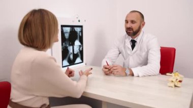 Doktor Danışmanlık, Doktor Muayenesi, Radyoloji Geçmişi. Klinikte, doktor, beyaz önlüklü, kadın hastasına omurilik röntgeni sonuçlarını açıklıyor..