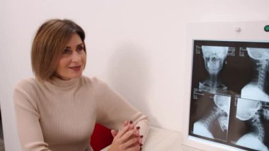 Kadın hasta, röntgen incelemesi, görüntüleme danışmanlığı. Beyaz önlüklü doktor, muayene odasındaki hastayla omurilik röntgenleri hakkında konuşuyor..