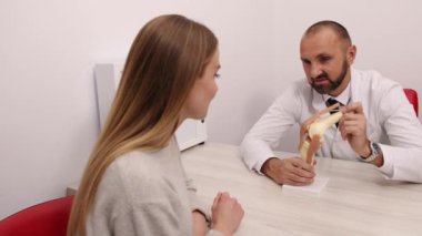 Diz bağı ağrısı, muayene odası, dizkapağı tendonu. Kadın hastalarla görüşürken, sağlık uzmanı diz anatomisini göstermek için model kullanıyor..