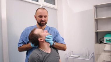 Servikal tedavi, kiropraktik seansı, oturma pozisyonu. Elleri başının arkasında oturan erkek hasta mavi önlüklü ve eldivenli kayropraktik uzmanı tarafından boynu düzeltiliyor..