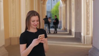Cep telefonu çalışıyor, cep telefonuyla meşgul, akıllı telefon kullanıyor. Siyah elbiseli genç kadın arka planda bulanık insanlarla dışarıda dururken akıllı telefon kullanıyor..