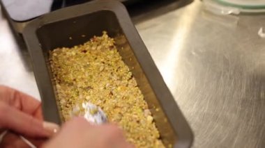 Tohum karışımı, kaşık karışımı, ev yapımı yemekler. Yakından bakıldığında, kişi kaşık kullanarak tohumları, fındıkları ve tahılları dikdörtgensel pişirme tenekesine basar..