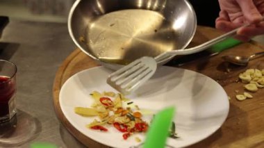 Sotelenmiş sarımsak, spatula kullanımı, yemek pişirme. Yakın çekim sarımsak, biber ve diğer sebzeler paslanmaz çelikten spatula kullanılarak beyaz tabağa aktarılıyor.