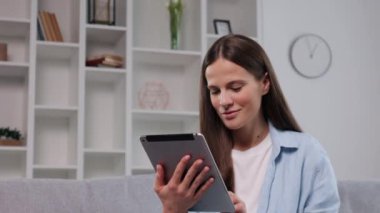 Boş zaman, rahat ev, modern dekor. Modern oturma odası, rahat gri koltukta otururken tablet kullanan genç bir kadın için sahne hazırlıyor..