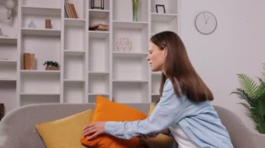 Kol ağrısı, kanepe sağlığı, kadın ağrısı. Kanepede oturan genç bir kadın, dirseğini tutuyor, kollarında acı dolu bir ifade, rahatsızlığı ya da sağlık sorununu gösteriyor..