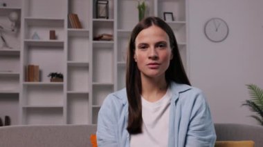 Kamera, kanepe portresi, huzurlu bir kadın. Kanepede oturan genç bir kadın, doğrudan kameraya bakıyor. Evde sakin ve sakin bir ifadeyle..