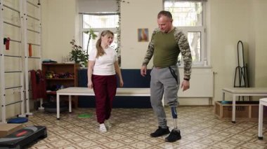 Uyarlamalı egzersiz, fitness protezi, protez eğitim. Terapi merkezinde yapay bacaklı bir adam antrenörü tarafından şınav çekilerek yönlendirilir..