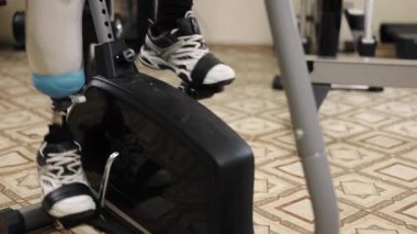 Egzersiz, spor egzersizi, fitness adaptasyonu. Yapay uzuvlu bir adam spor salonunda bacak pres makinesi üzerinde egzersiz yapıyor, diğer ekipmanlar etrafa saçılıyor..