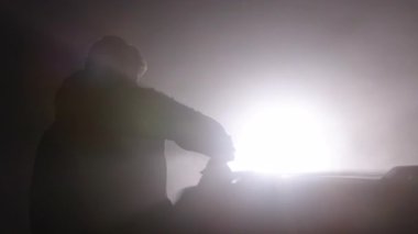 Otomobil tamiri, sağlık riskleri, boya katkı maddeleri. Arka planda, sisli arka planda kalan arabayı sprey boyayla boyarken, çarpıcı bir siluet kalıbı var..