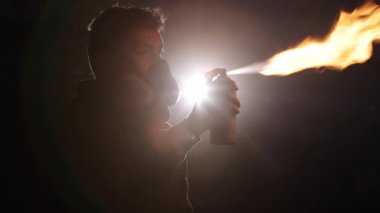 Ateşleme sanatı, güvenlik önlemleri, yangın yaratma. Koyu, dumanlı çerçeveler siluetli kişi canlı alevler yaratmak için aerosol kullanıyor ve koruyucu gaz maskesi takıyor..