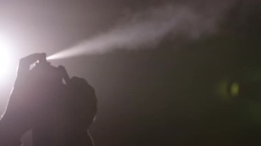 Yangın gösterisi, yangın güvenliği, havai fişek sanatı. Gölgeli, sisli ortamda, siluet, güvenlik için koruyucu maske ile donatılmış etkileyici bir alev yaratmak için sprey kullanır..