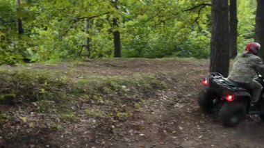 Farlar açık, off-road sürücüsü, kask koruması. Kamuflaj ve miğfer takan ATV sürücüsü, sık ormandaki toprak yolda manevra yapıyor..