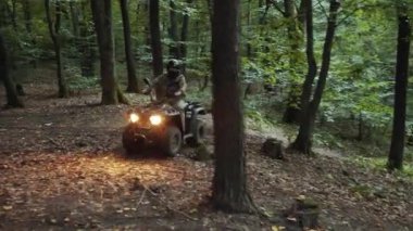Arazi gezgini, Trail Macerası, Yoğun Orman. Kamuflajlı miğferli sürücü, sık ormanda toprak patika boyunca ATV sürüyor, yol ışıklarıyla aydınlanıyor..