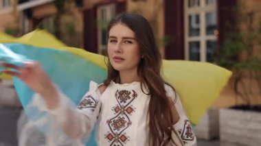 Eski şehir, şehir manzarası, halk kostümü. Klasik şehir sokaklarında, kendine güveni tam geleneksel Ukrayna bluzu giymiş genç bir kadın mavi ve sarı bayrağını sallıyor.