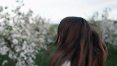 Tekrar kontrol ediyorum, Koşu yolu, Yeşil Manzara. Çiçekli çimen ve çiçek açan ağaçlarla dolu bir bahçede kadın koşar, gülümser ve geriye bakar..