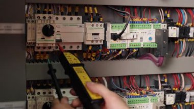 Çoklu kullanım, devre tamiri, elektrik güvenliği. Detaylı görüntü elektrikçisi elektrik bağlantılarını çoklu metre ile kontrol ediyor. Devre kesici paneli canlı kablolarla dolu..