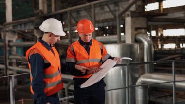 Mühendis konsültasyonu, tasarım onayı, alan planlaması. Fabrika ortamında, mühendis planları analiz etmek için inşaat işçisiyle işbirliği yapıyor..