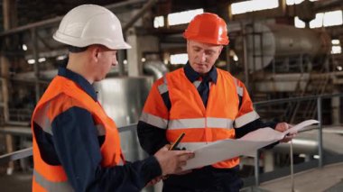 Site planlama, çizimleri gözden geçirme, şemaları denetleme. Teknik planlar fabrikadaki mühendis ve inşaat işçisi tarafından inceleniyor..