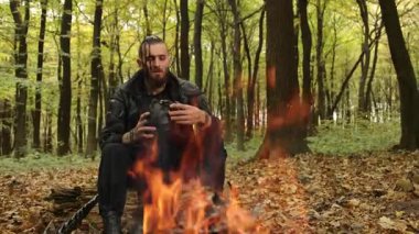 Hayatta kalma içkisi, taktik teçhizat, orman şişesi. Ormanda kamp ateşinin yanında oturup kendine güvenme ve dayanıklılığı vurgularken mataradaki dayanıklılık içeceklerini içen engebeli bir hayatta kalma ustası..