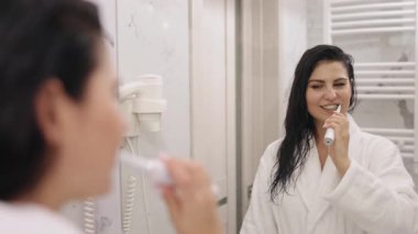 Aynaya bak, Bornoz Kadın, Diş fırçalama. Güzel bir kadın, duş aldıktan sonra, dişlerini fırçalar, banyo aynasında kendine bakar, beyaz giyinir, bornoz giyer.