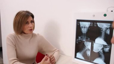Tıbbi İnceleme, Hasta Bakımı, Sağlık Danışmanlığı. Kadın hasta, beyaz önlüklü doktoru klinikte omurga röntgenlerini yorumlarken dikkatle dinliyor..