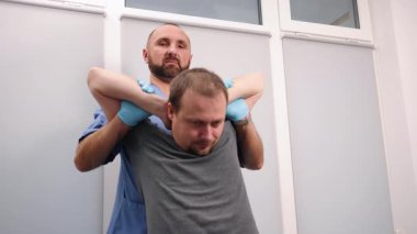 Kayropraktik boyun bakımı, hasta terapisi, omurga düzeltmesi. Mavi önlük ve eldiven giyen kayropraktik uzmanı, elleri başının arkasında oturan erkek hastanın boynunu düzeltir..