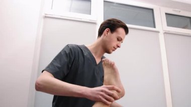 El terapisi, kayropraktik uzmanı ayarlaması, sağlık seansı. Koyu renk önlükler giyen kayropraktik uzmanı, tedavi masasında yatmakta olan erkek hastaya bacak ayarlaması yapıyor..