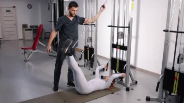 Bacak esnetme, iyileşme eğitimi, rehberli esneme. Erkek fizyoterapist, kadın hastaya spor salonu temelli rehabilitasyon sırasında bacak esnetmesinde yardım ediyor..
