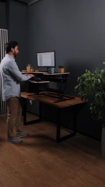 Dik masa, ofis masası, modern bitkiler. Ahşap zemin ve bitkilerle modern ofiste, açık mavi gömlekli adam monitörlü, dikey video masasında çalışıyor..