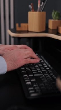 El yazısı, arama ve sörf, modern ofis. Yakın plan, modern ofis ortamında ahşap düzenleyiciler ve küçük bitkilerle süslenmiş şık bir masada siyah klavyeye yazı yazan elleri yakalıyor. Dikey