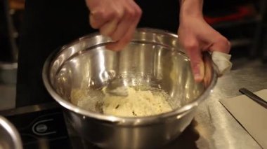 Karıştırıcı malzemeler, karıştırma kabı, metal kase. Kaşık kullanarak büyük metal karıştırma kabının içindeki malzemeleri karıştıran yakın plan insan. Tarifi hazırlarken insanların elleri görünürde, kaseyi sabit tutuyorlar.
