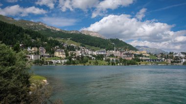 The mountain lake of St. Moritz with the fashionable alpine resort in the background on a nice summer day clipart