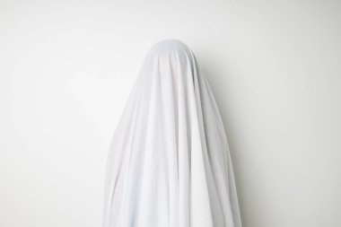 Beyaz arka plandaki hayalet gibi beyaz bir çarşafla kaplanmış bir kadın..