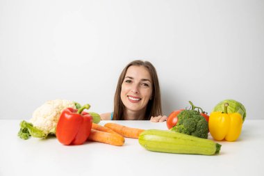 Masanın altından taze sebzelere bakan gülümseyen genç bir kadın..
